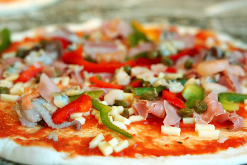 Pizza Quattro stagioni en préparation: fruits de mer, jambon de devant, poivrons et câpres.